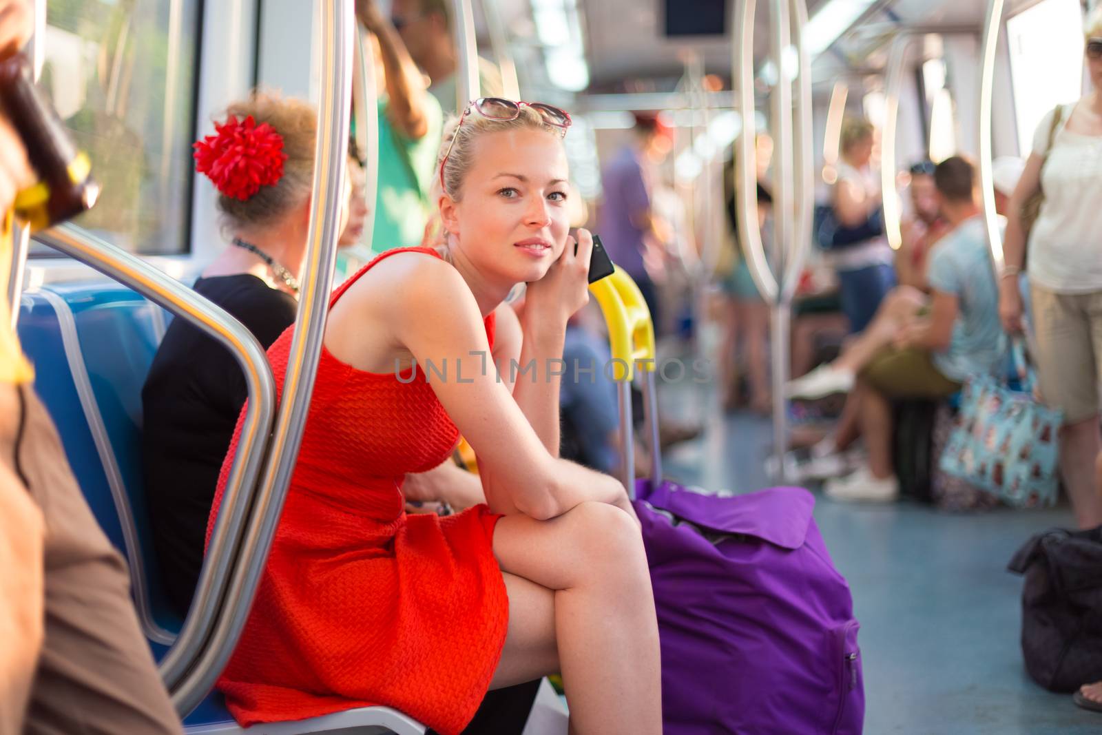 Beautiful blonde caucasian lady in red dress traveling by metro.