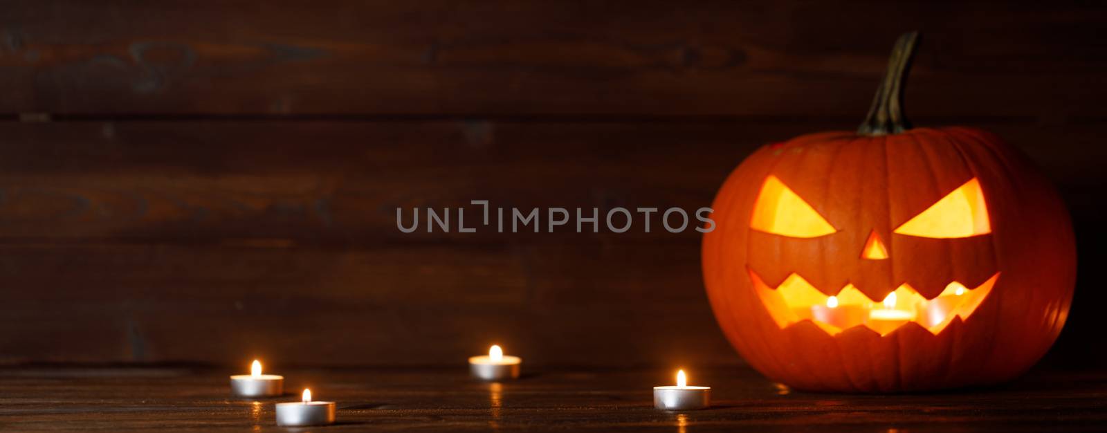 Halloween pumpkin head jack o lantern and candles on wooden background