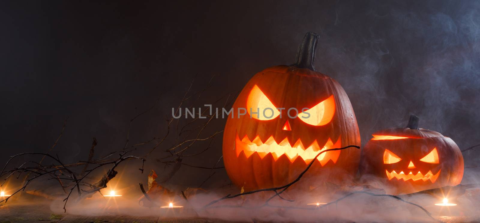 Halloween pumpkin heads jack o lantern and candles in fog on wooden background