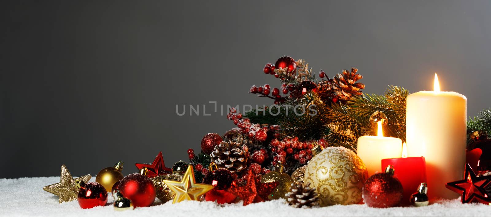 Burning christmas candles with red and golden decorative stars , baubles , pine cones and green branches on snow