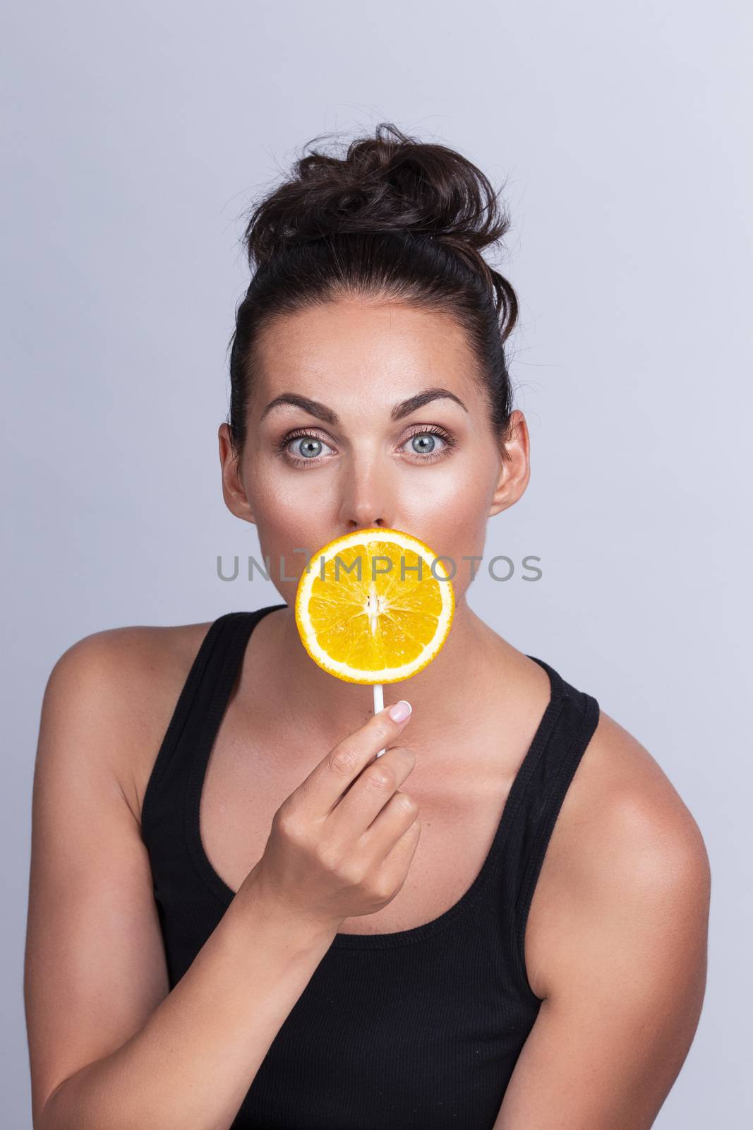 Portrait of beautiful woman with perfect skin holding orange slice on stick