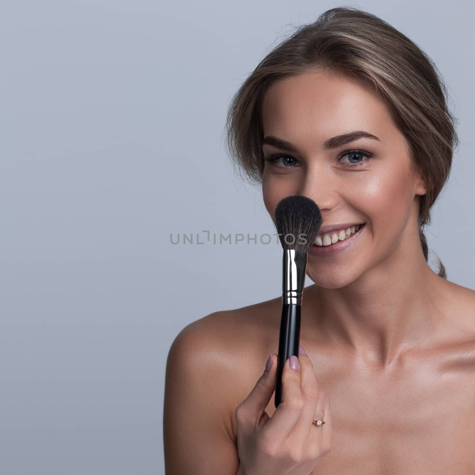 Portrait of beautiful woman smiling holding makeup brush on gray background