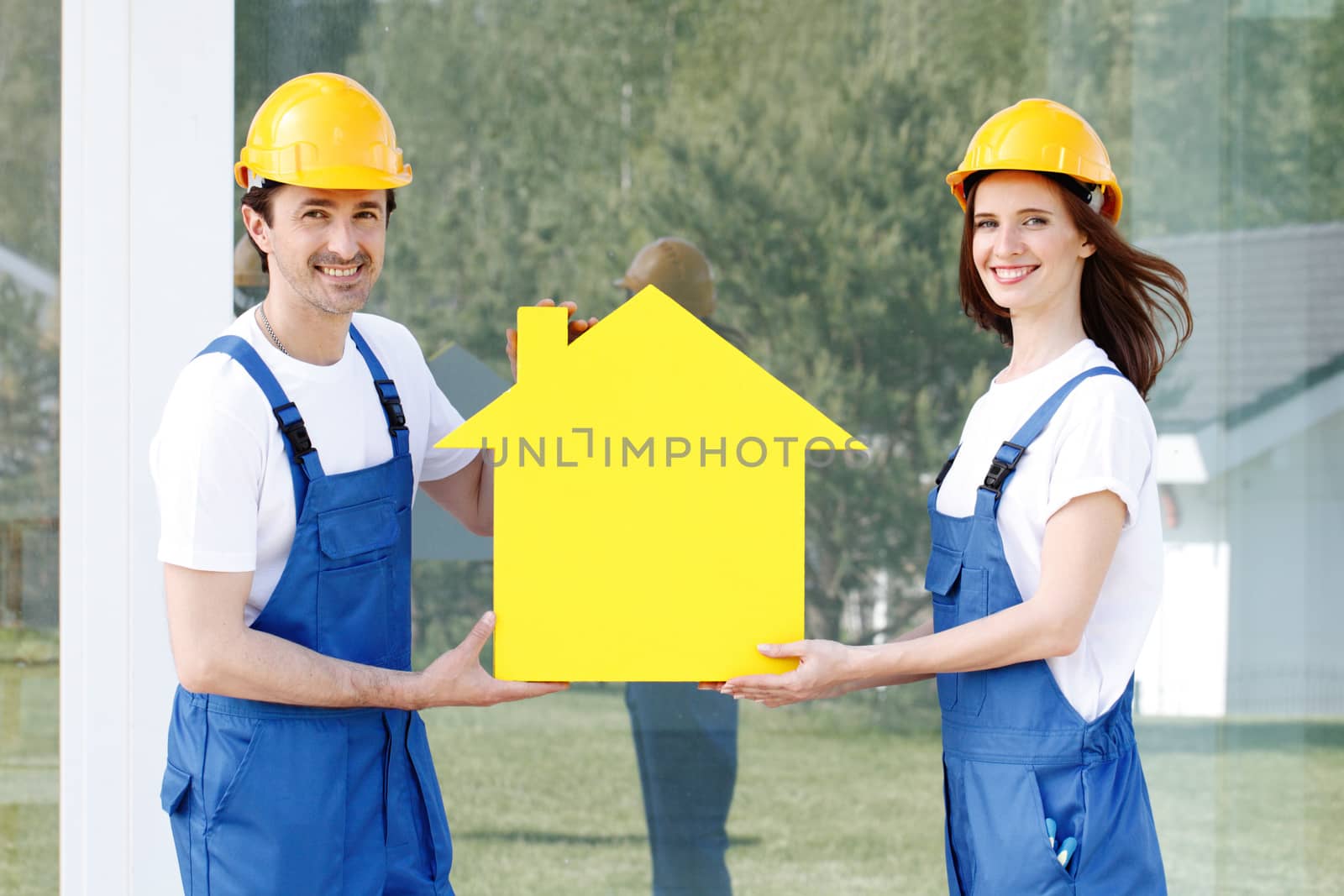 Two happy smiling workers hold yellow house model outdoors at construction site