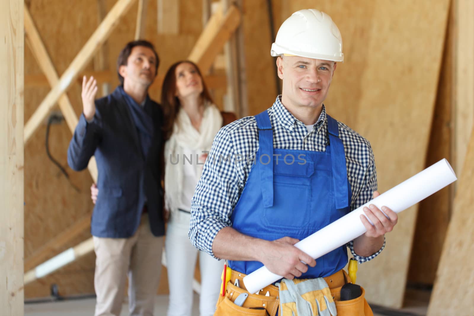 Foreman with house design plans and young couple at construction site