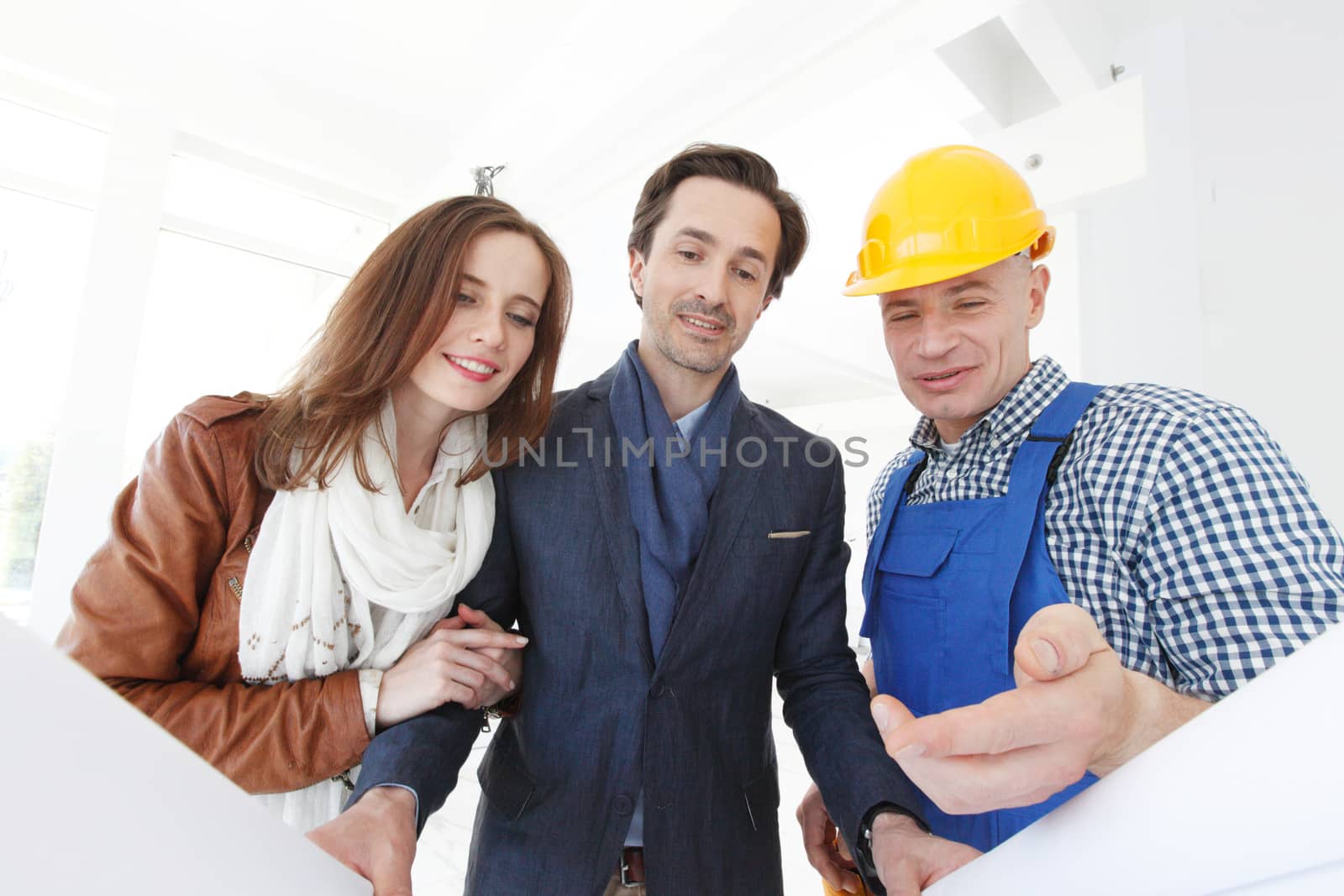 Foreman shows house design plans to a young couple at construction site