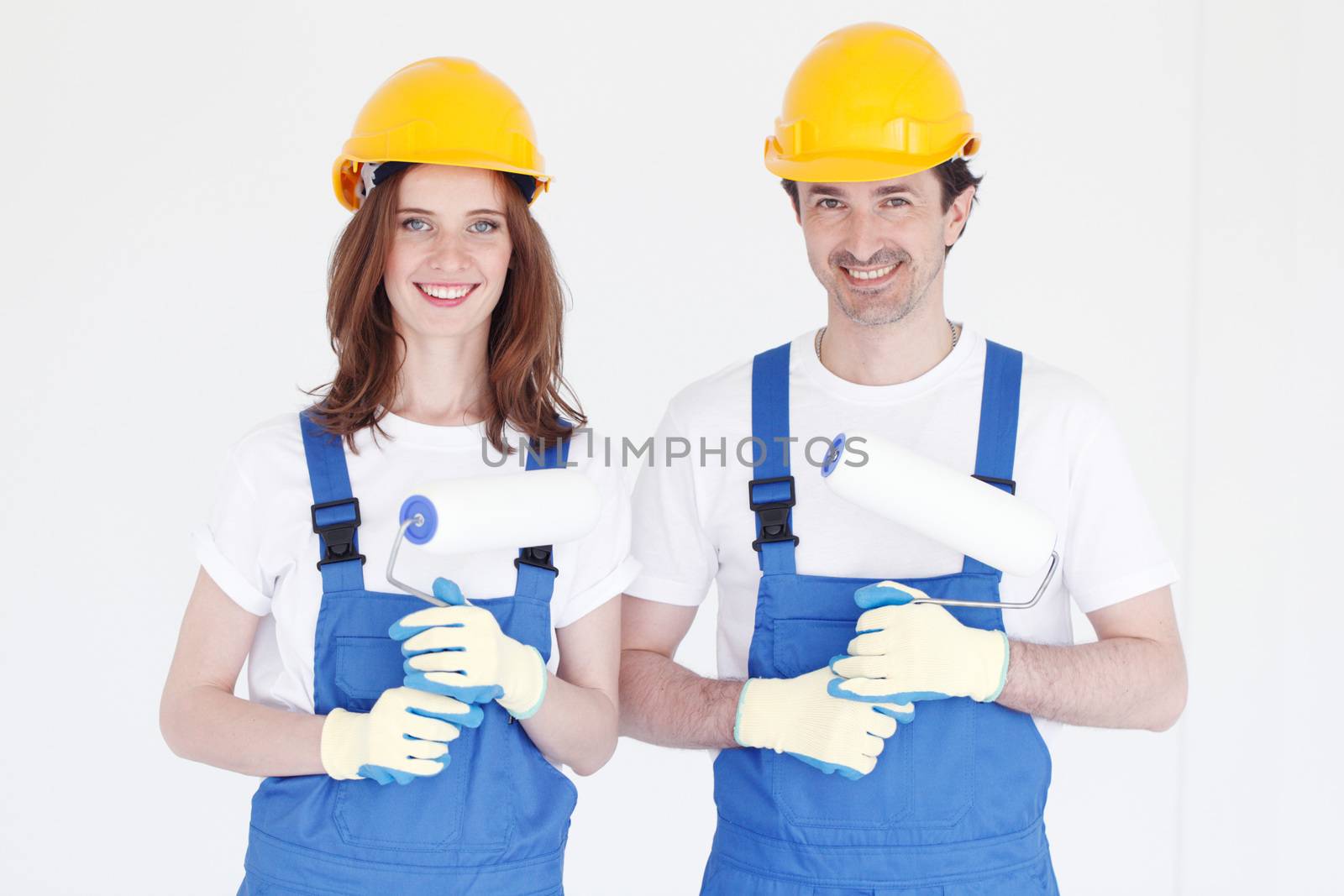 Happy young couple in uniform with with paint rollers in their new house. Repair, construction and mortgage concept.