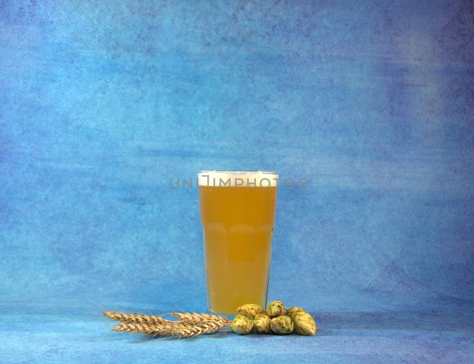 Glass of wheat beer with hops and sprinkles on a blue abstract background. Close-up.