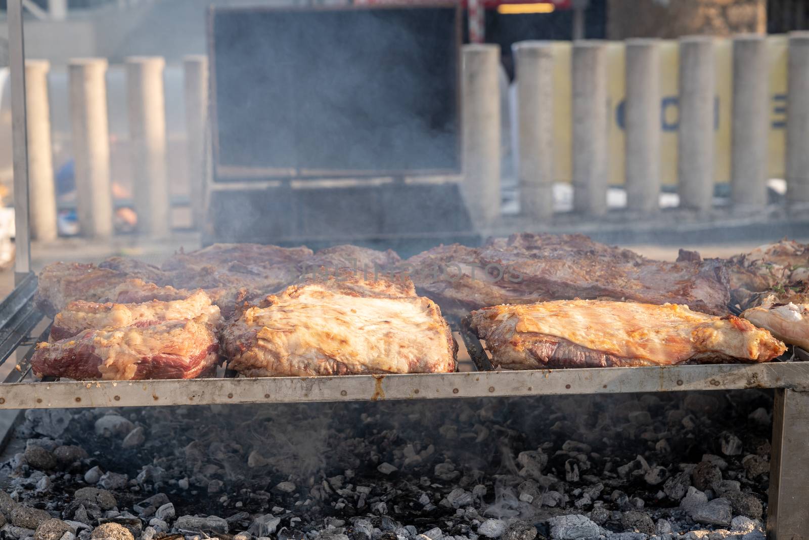 BBQ beef lined up on a large outdoor grill with smoke coming up from the fire below.