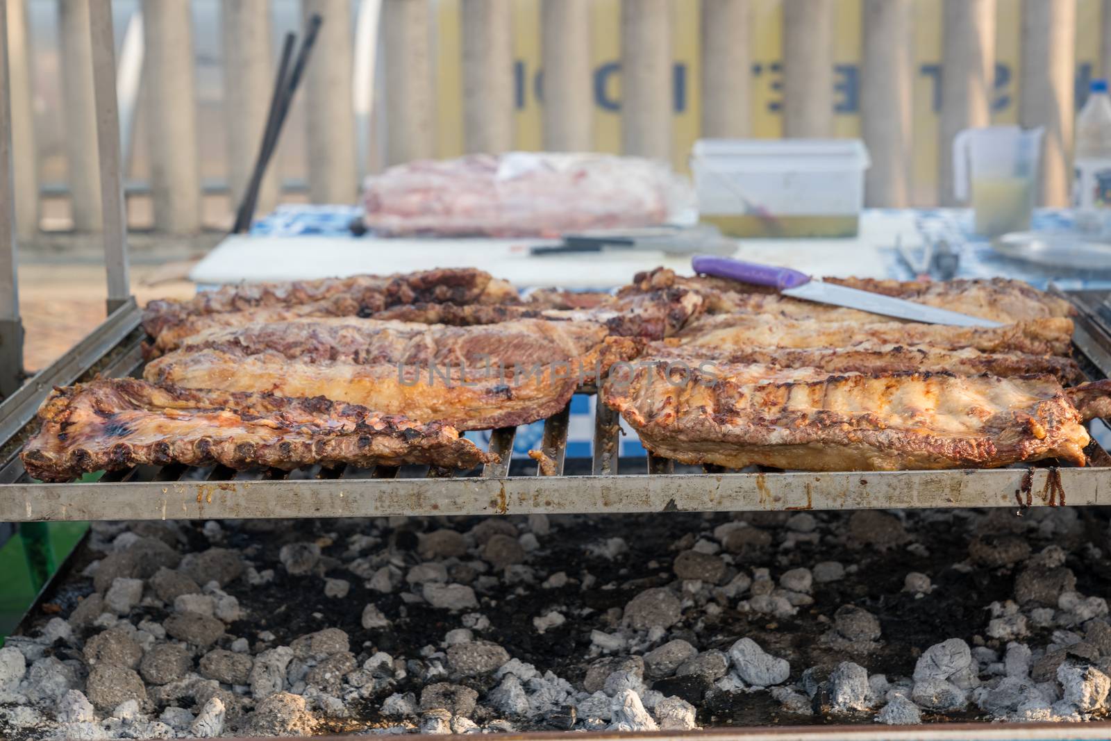 BBQ rack of pork ribs lined up on a large outdoor grill with smoke coming up from the fire below.