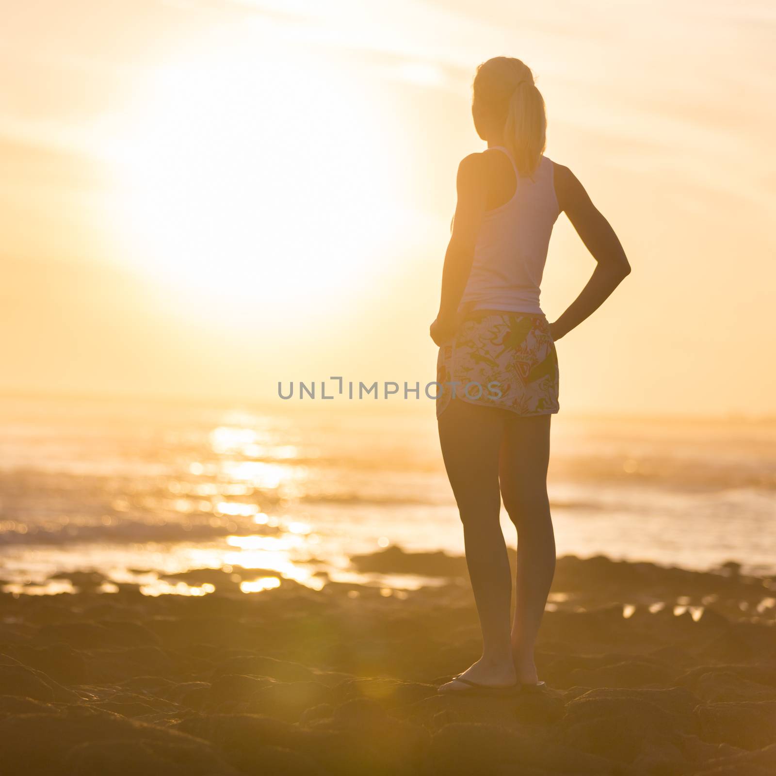 Silhouette of meditative, sensual blonde woman watching sunset at the beach.