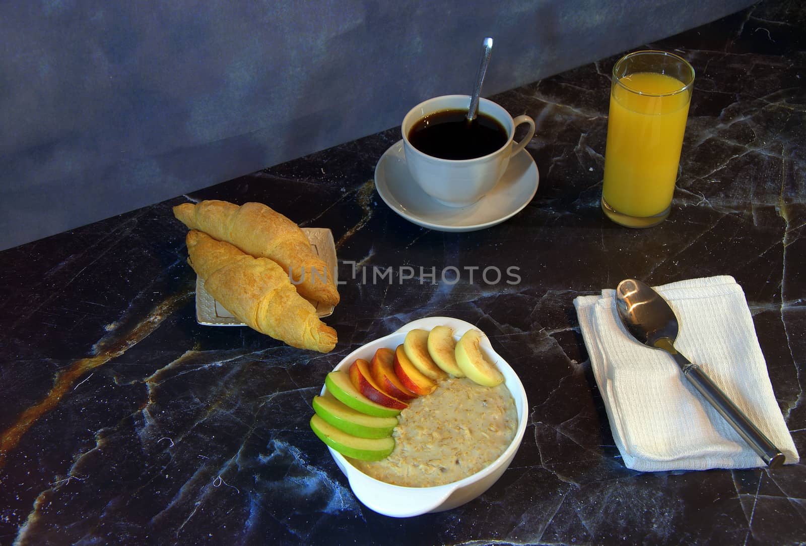 Healthy breakfast, a cup of oatmeal with slices of fruit, a glass of orange juice, black coffee and two croissants. Close-up.