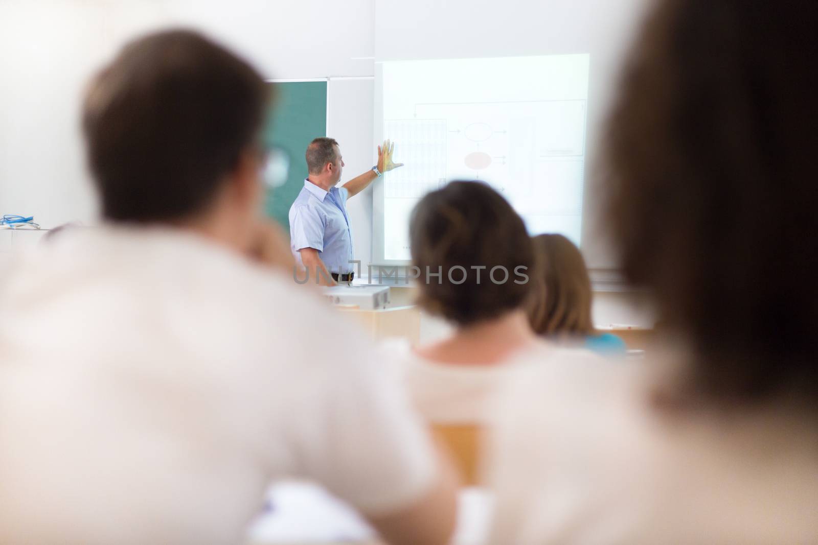 Teacher at university in front of a whiteboard screen. Students listening to lecture and making notes.