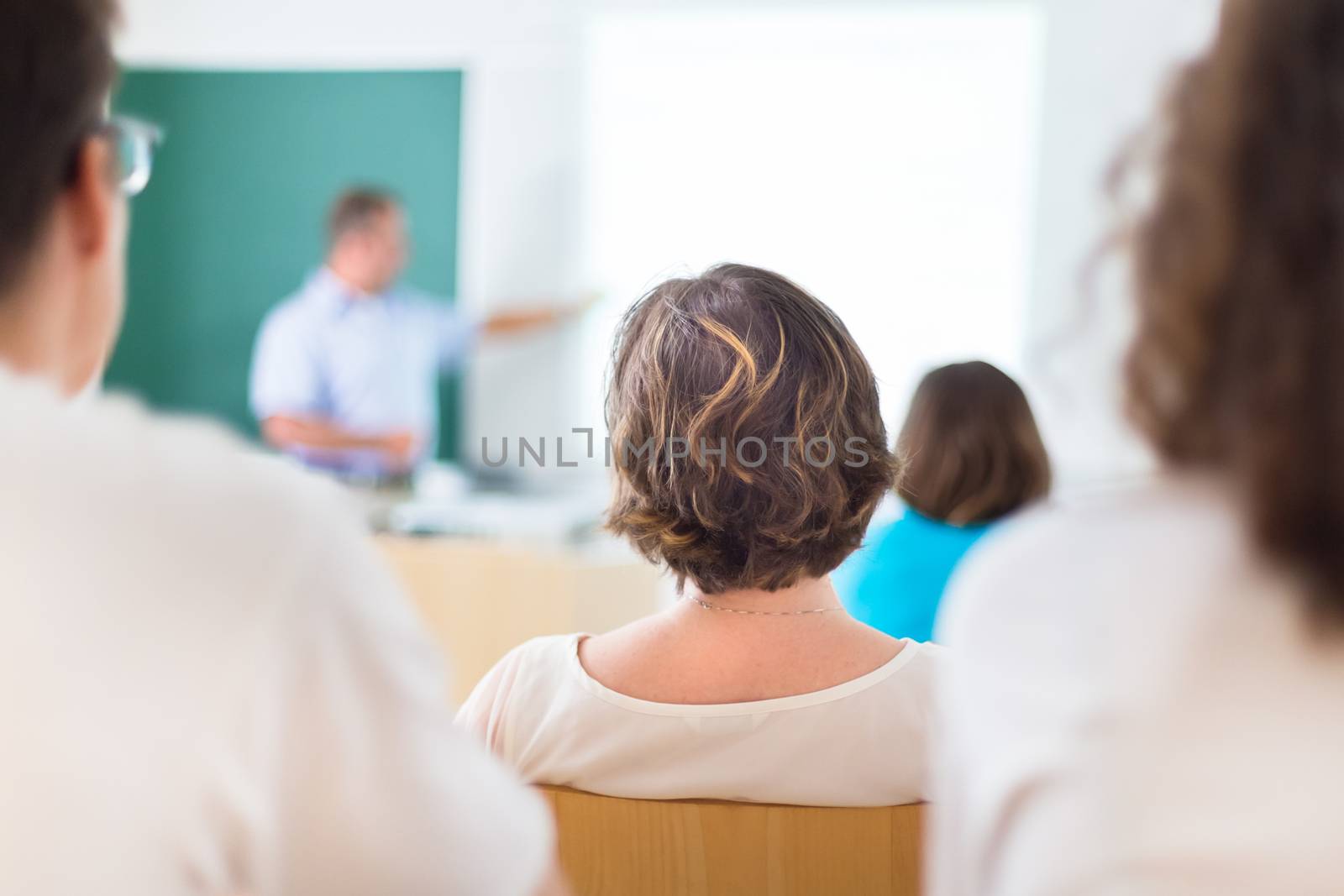 Teacher at university in front of a whiteboard screen. Students listening to lecture and making notes. Focus on the student.