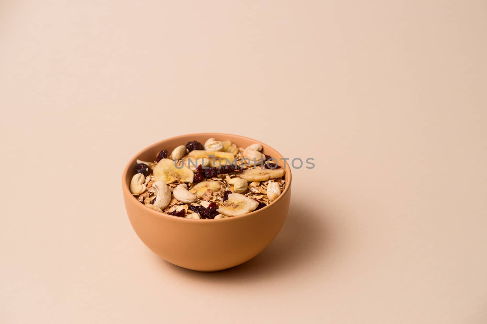 A fresh granola with dried and candied nuts and fruits in beige colour bowl closeup on beige bakground. Concept of nutrient and healty breakfast or meal
