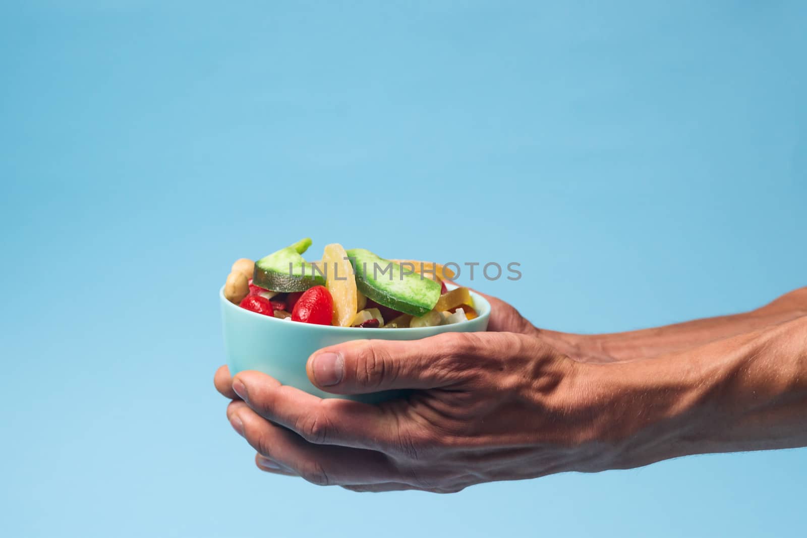 Male hands holding a full bowl of candied fruits and nuts on blu by alexsdriver