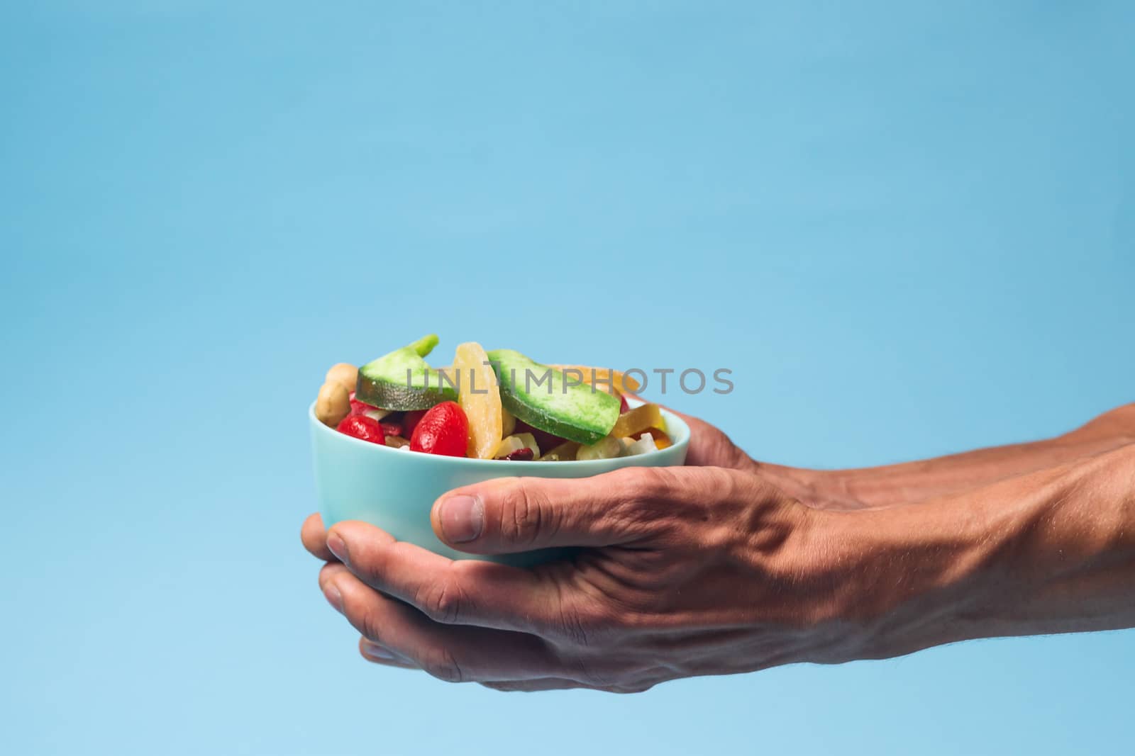 Male hands holding a full blue bowl of candied fruits and nuts on blue background. Stock photo of nutrient and healty food. Conceptual photo of vegan and vegetarial food and meal.