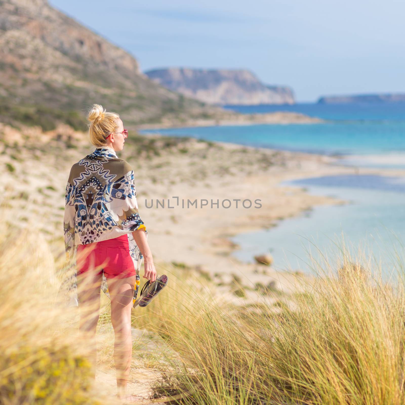Relaxed woman wrapped in colorful scarf, enjoying sun, freedom and life at beautiful Balos beach in Greece. Concept of holidays, vacations, freedom, joy and well being.