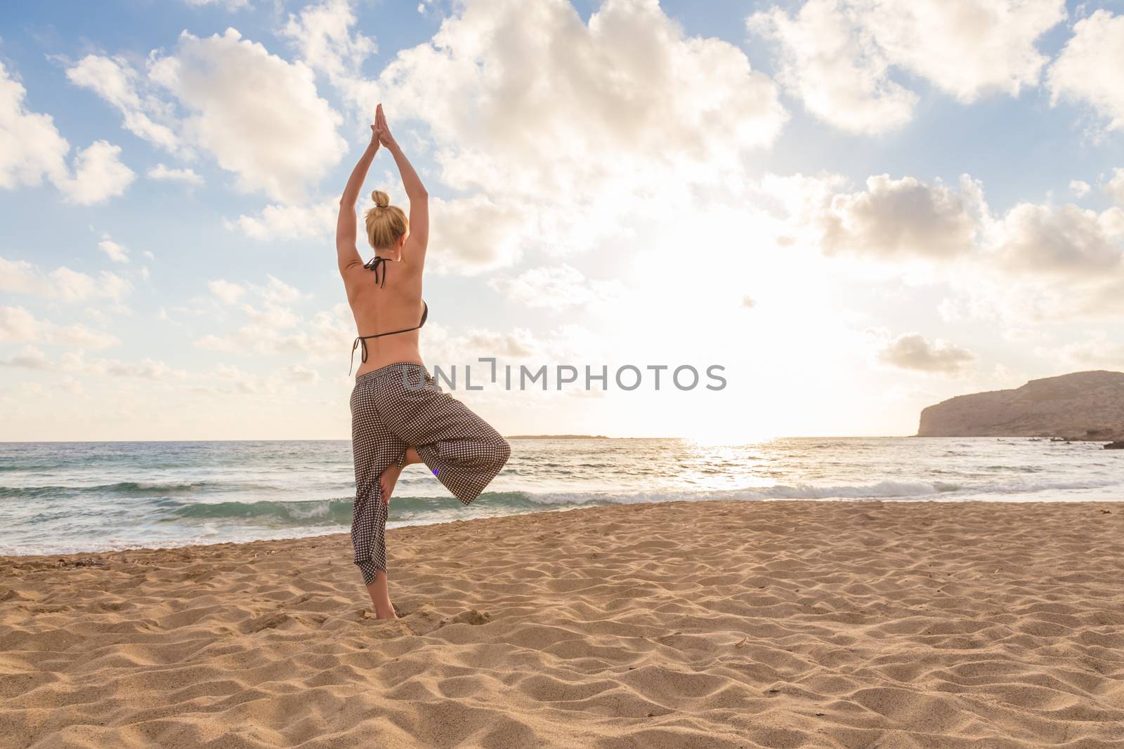 Active young woman practicing yoga on beach at sunset.