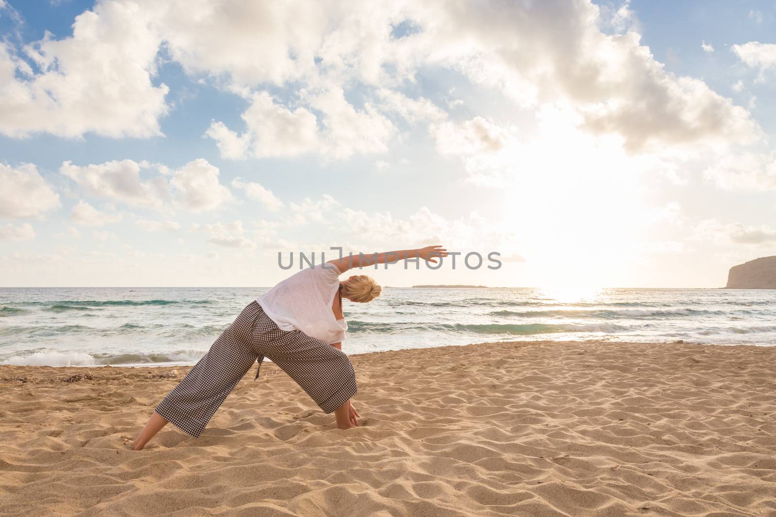 Active young woman practicing yoga on beach at sunset.