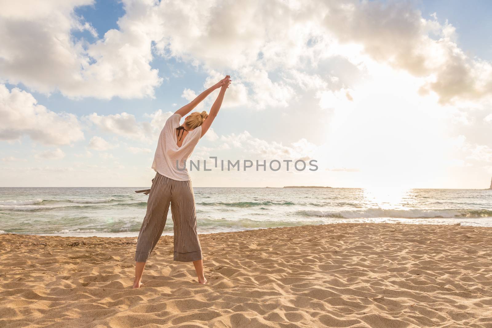 Active young woman practicing yoga on beach at sunset.