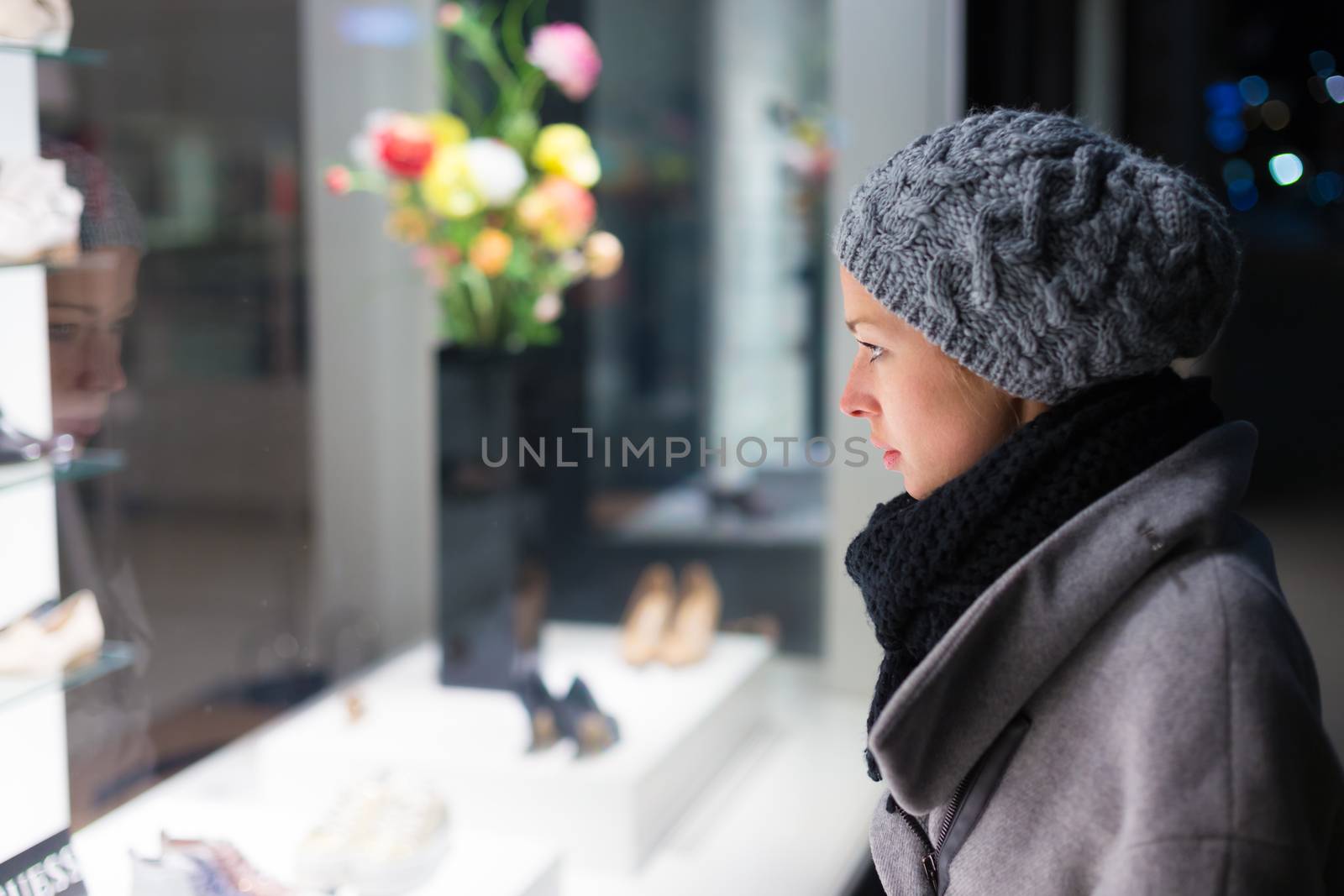 Casualy winter dressed lady window shopping in front of sinfully expensive boutique store dispaly window. Customer woman in shopping street, looking at window, outdoor.