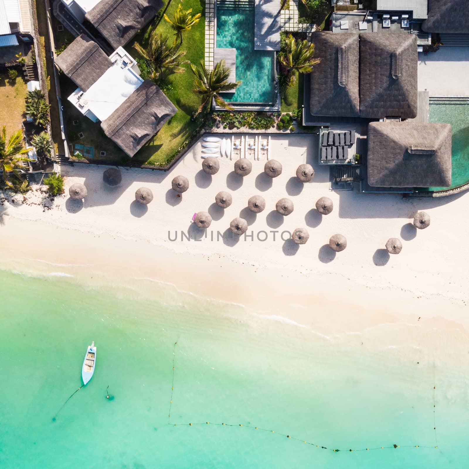 Aerial view of beautiful tropical beach front hotel resort with swimming pool, palm leaves umbrellas and turquoise sea. Paradise destination for vacations in Mauritius.