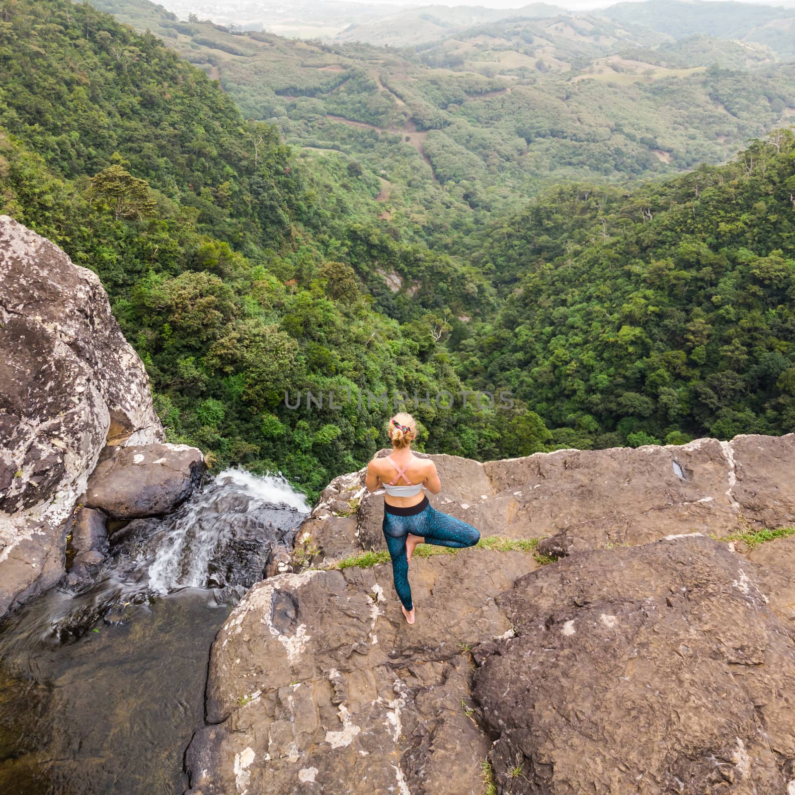 Active sporty woman relaxing in nature, practicing yoga on high clif by 500 feet waterfall at Black river gorges national park on tropical paradise island of Mauritius by kasto