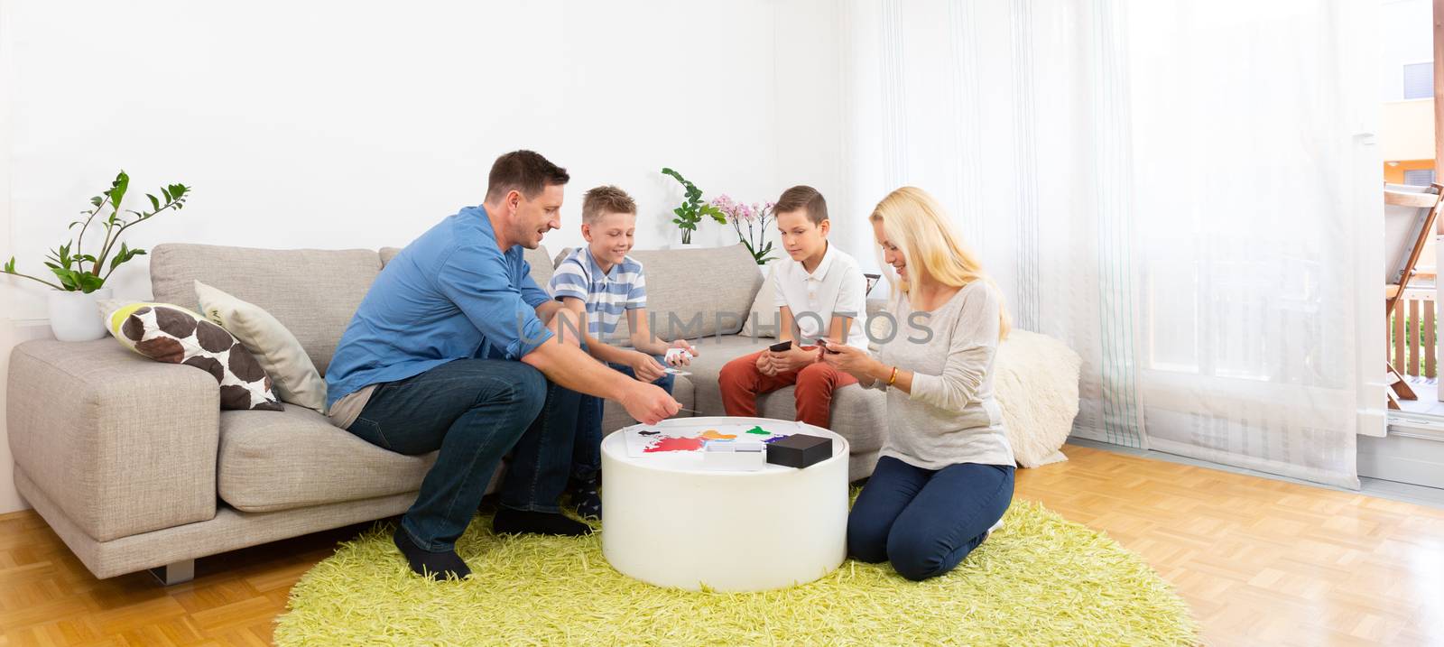 Happy young family playing card game on living room sofa at home. Spending quality leisure time with children and family concept. Cards are generic and debranded.