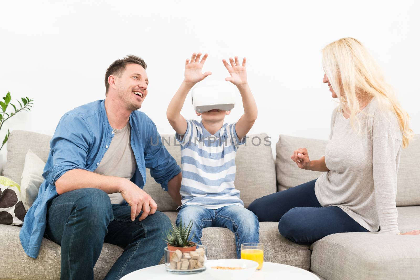 Happy caucasian family at home on living room sofa having fun playing games using virtual reality headset.