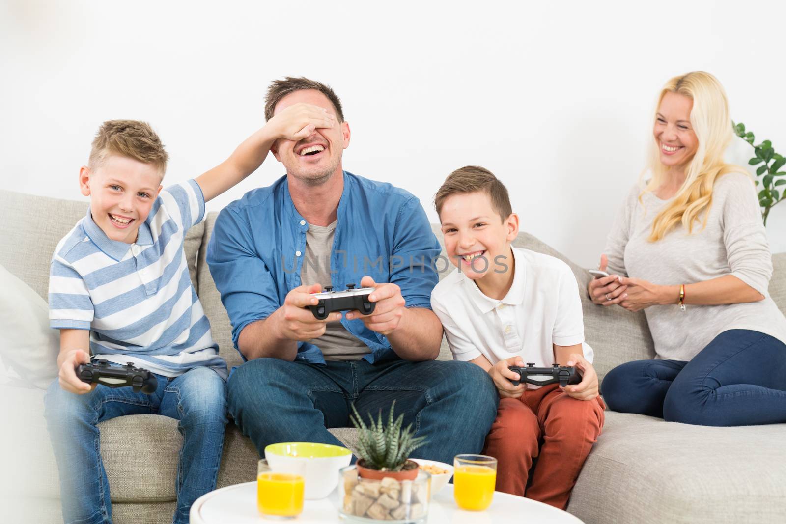 Happy young family playing videogame console on TV. Spending quality leisure time with children and family concept. Gaming consoles are generic and debranded.