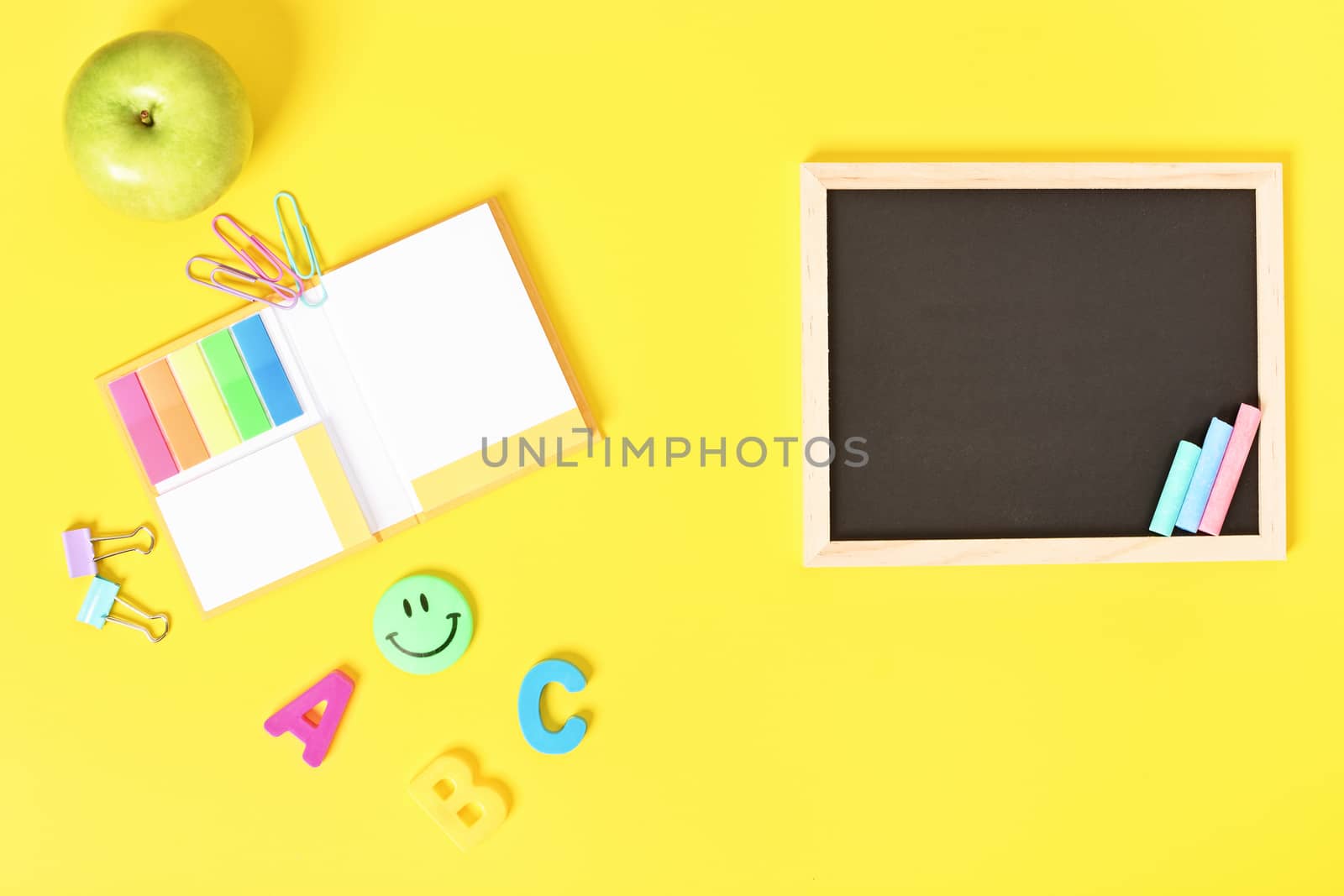 Chalkboard with wooden frame and colorful chalks and school stationeries, isolated on yellow background.