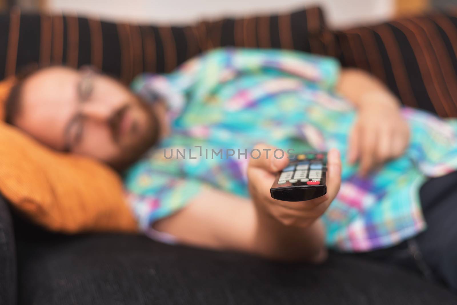 Man relaxing in sofa with remote control watching tv. Shallow dof focus on remote control. by HERRAEZ