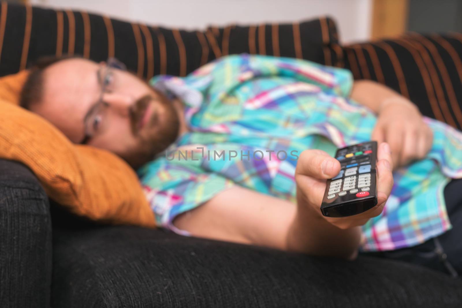 Man relaxing in sofa with remote control watching tv. Shallow dof focus on remote control.