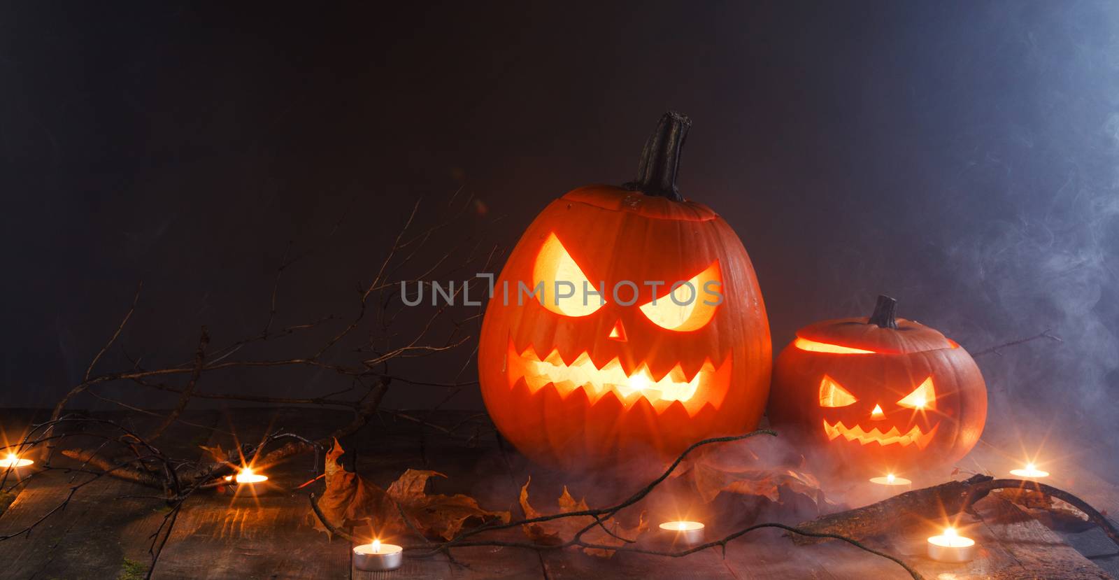 Halloween pumpkins head jack o lantern, candles and dry maple leaves in mist
