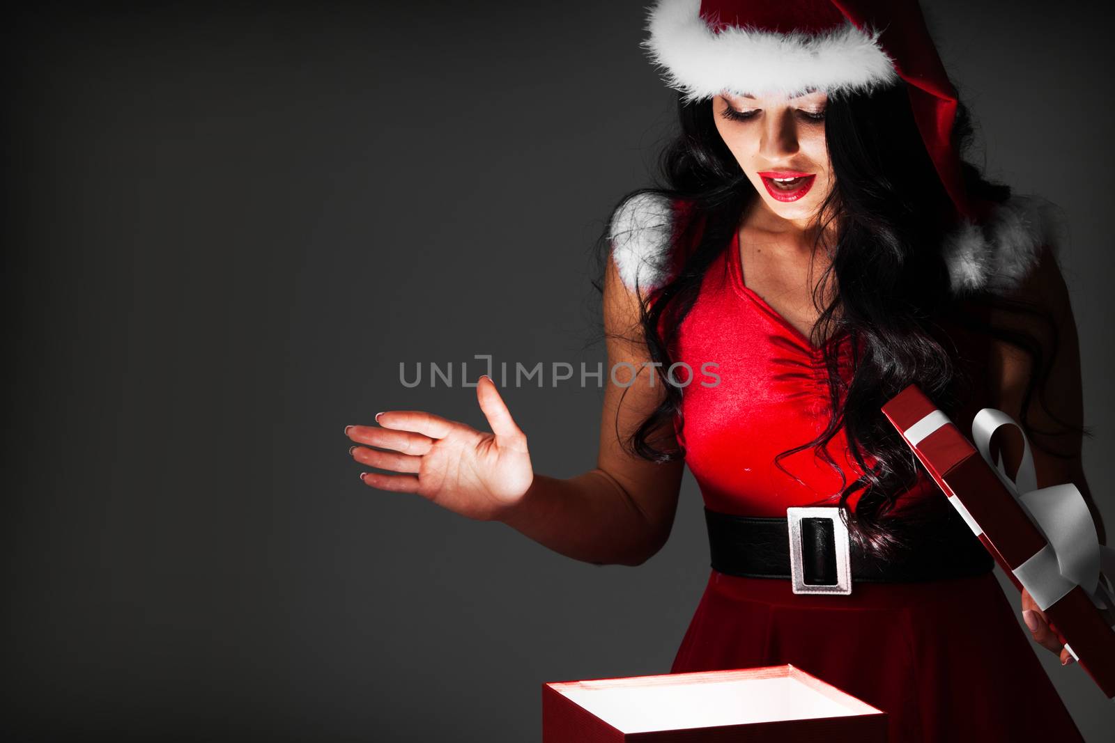 Beautiful woman in Santa Claus style costume looking into glowing Christmas gift box