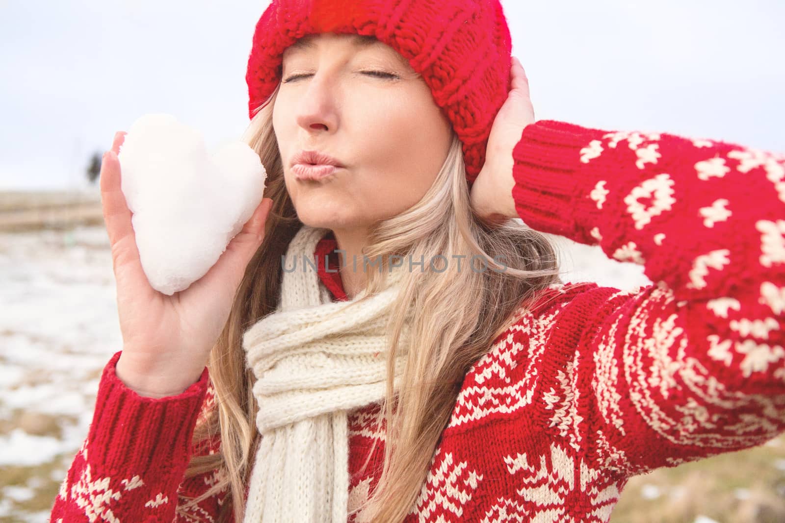 A female holds a snow ball in the shape of a heart and blowing kisses