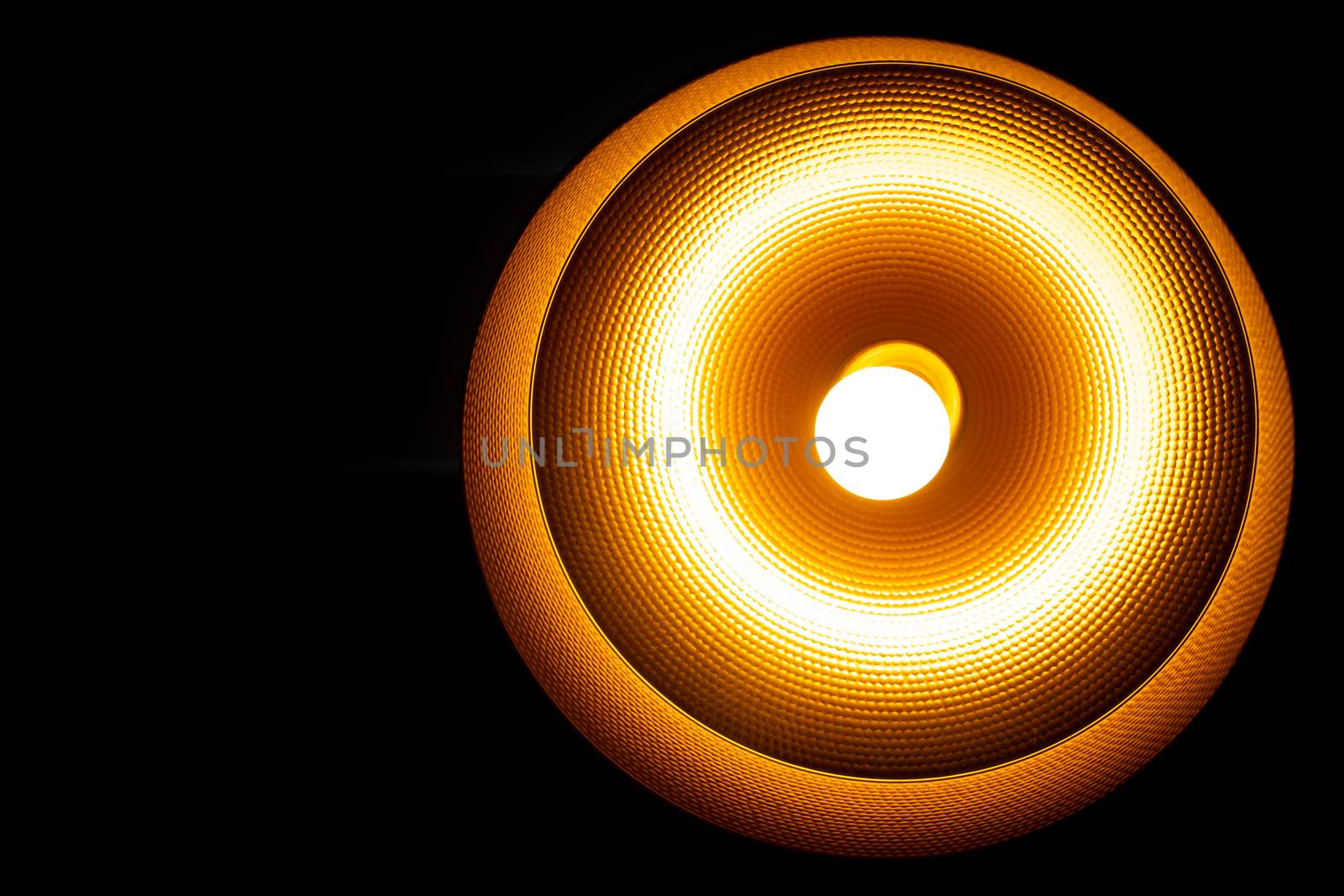 Modern lamp hanging down from ceiling in the dark background. Minimalist chandelier with glowing warm light from bulb.