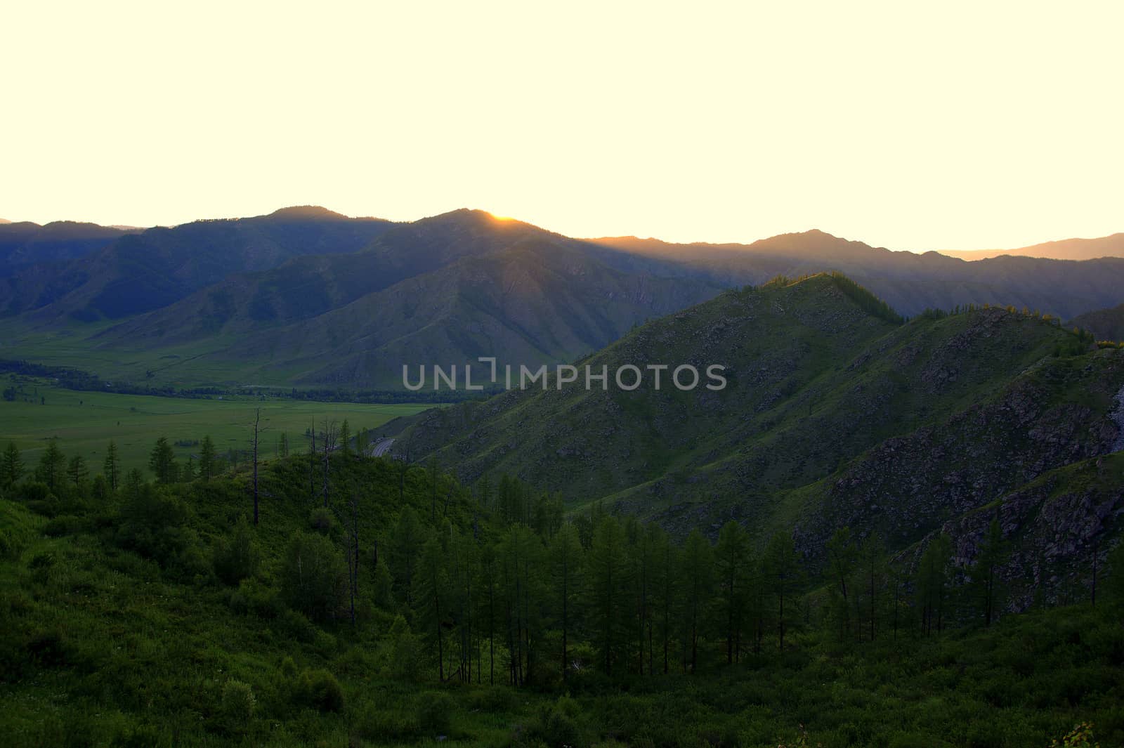 The evening landscape, the setting sun hid behind high mountains, illuminating the picturesque valley with its rays. Altai, Siberia, Russia.