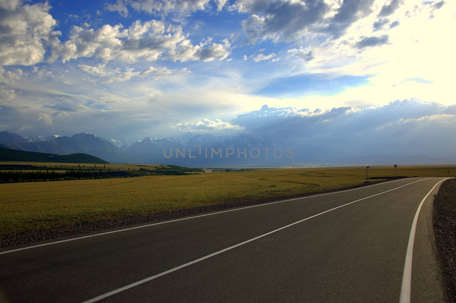 A direct asphalt road crossing a valley at the foot of snowy mountain ranges. by alexey_zheltukhin