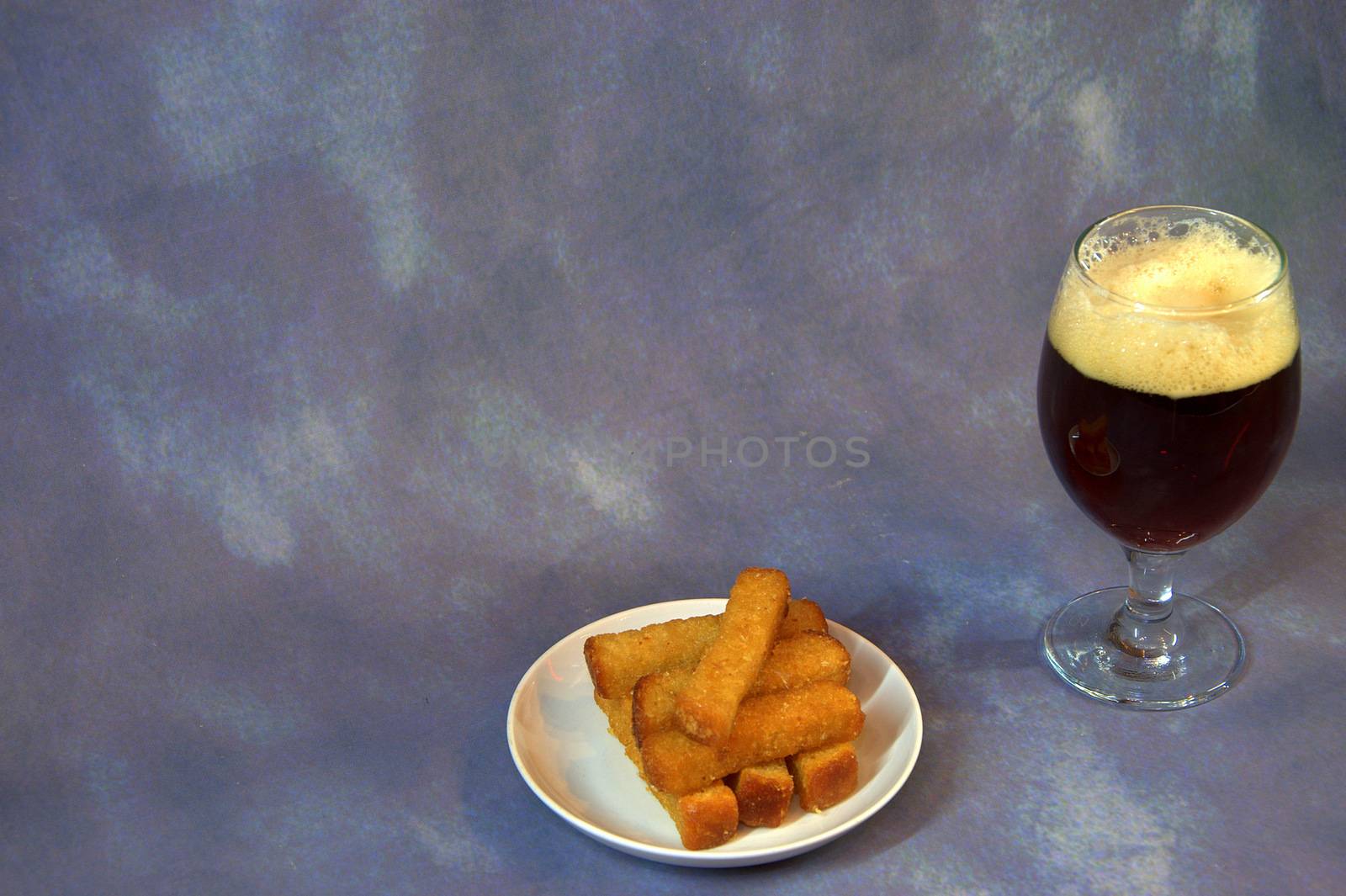 A glass of dark beer with foam and wheat croutons on a plate. Close-up.