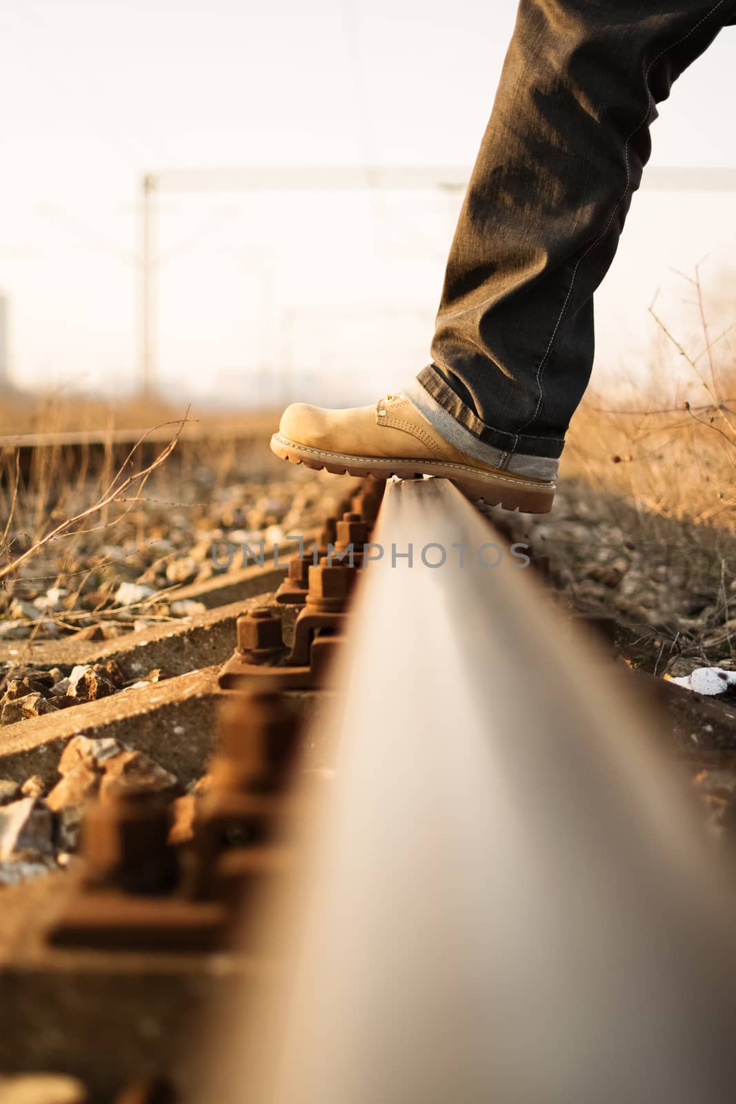 Time for a new journey. Man's foot stepping over train tracks.
