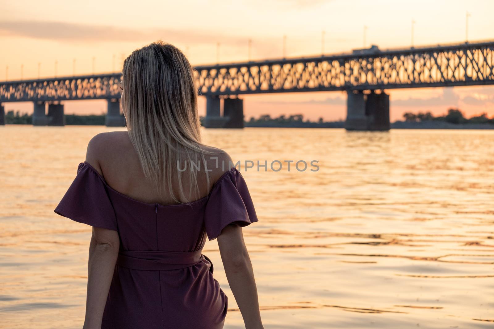 A young, beautiful and slender girl rides on the Amur river. Looking at the big bridge across the river