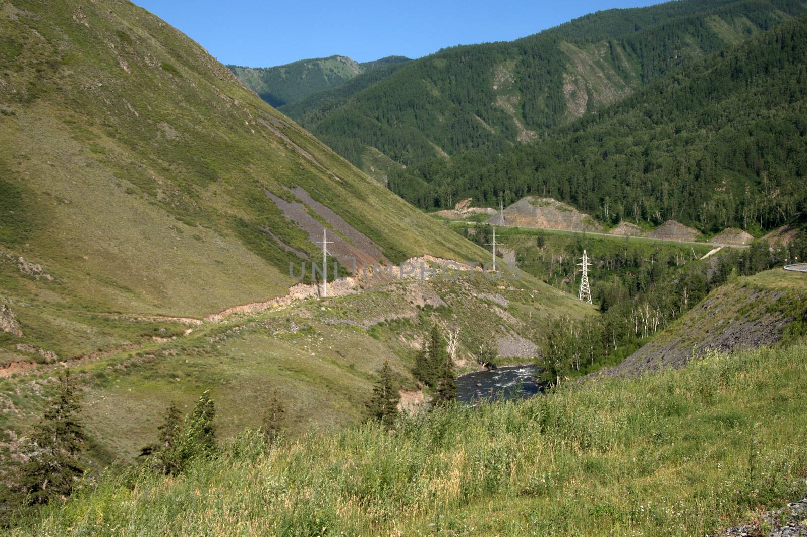 A power line stretching through a picturesque valley at the foot of a forested mountain.