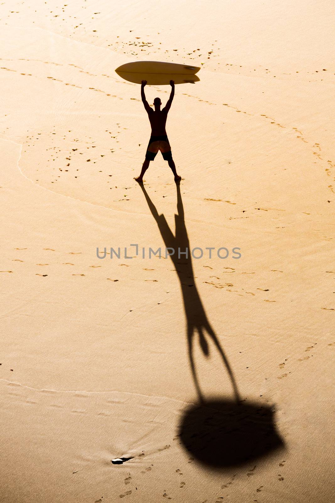 Top view of a surfer on the beach holding a surfboard