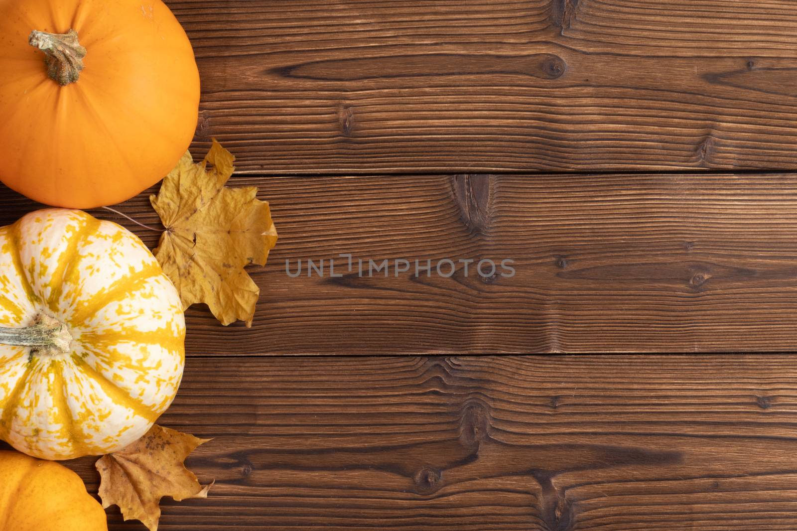 Striped yellow and orange pumpkins and dry maple autumn leaves on wooden background, top view, Halloween concept