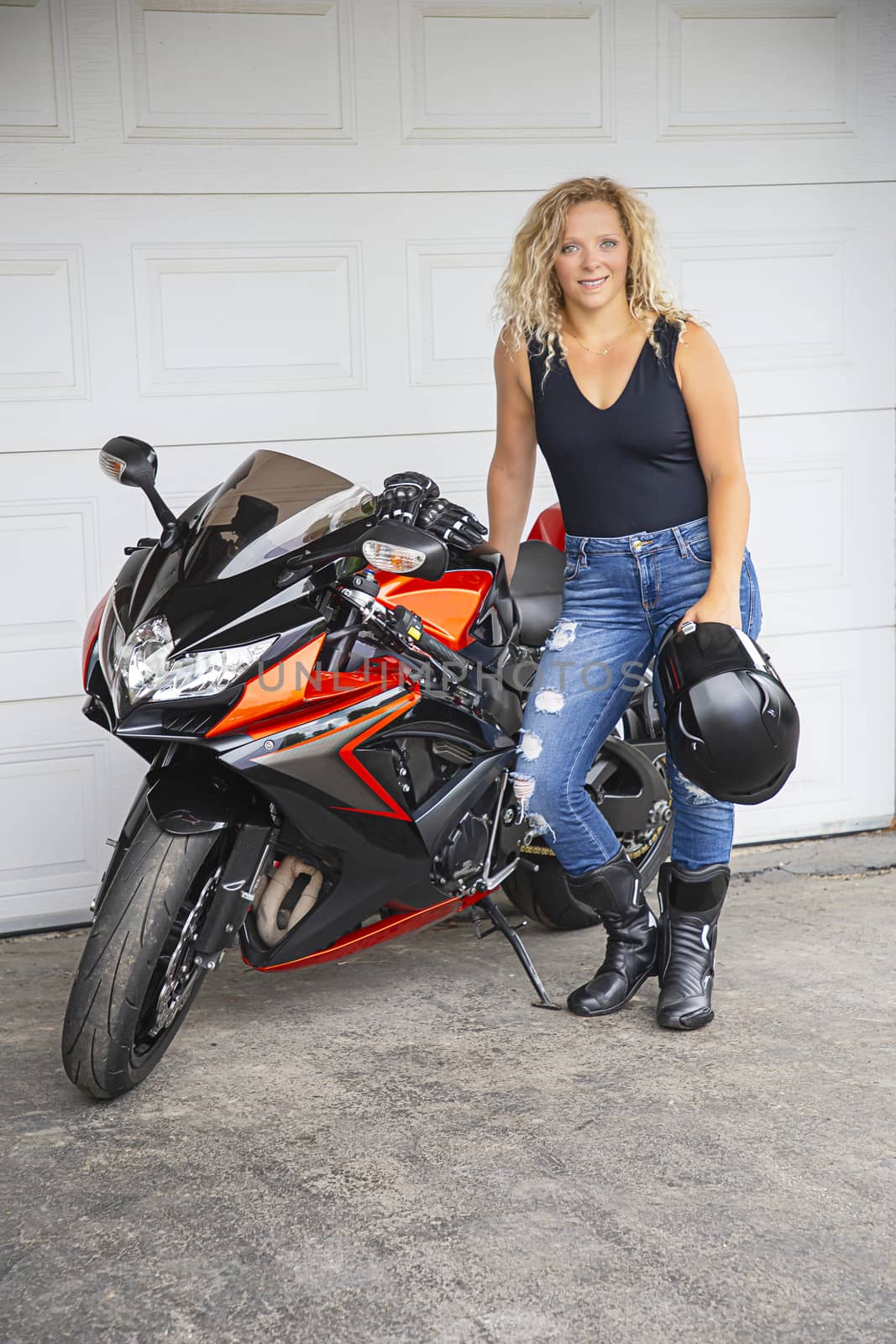 twenty something woman, leaning on a sport motocycle, standing in front of a garage door