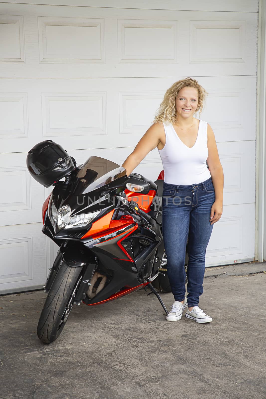 twenty something blond woman, leaning on a black and orange sport motocycle