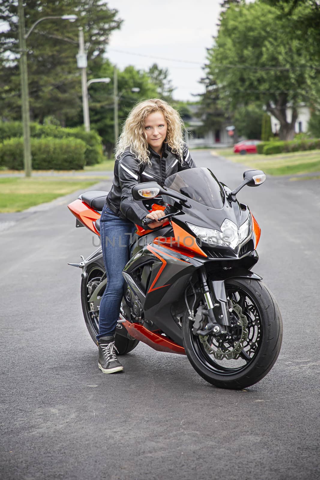 young blond woman, ready to ride a sport motocycle, in the middle of a suburb street
