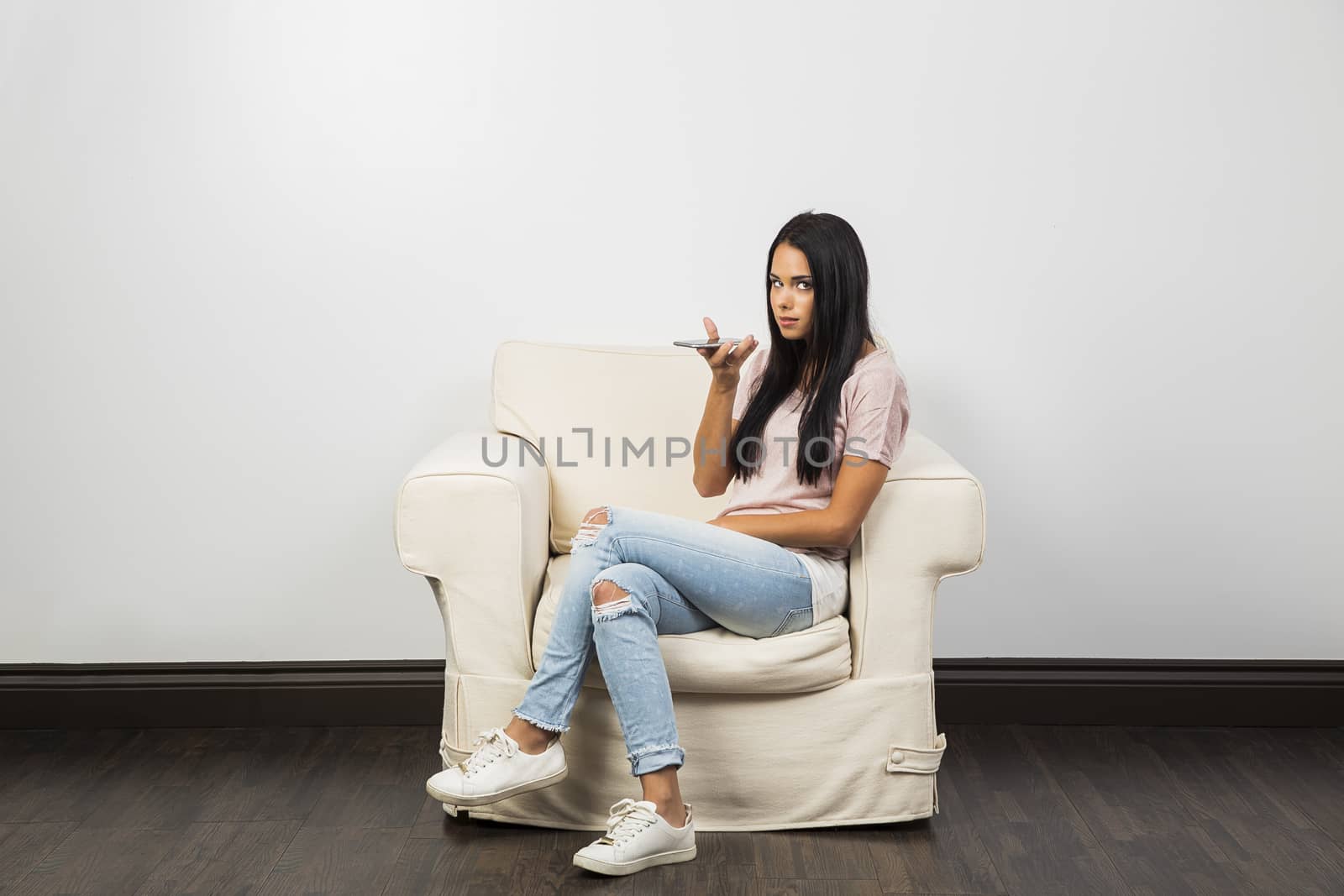 young woman, sitting on a white couch, talking on smart phone