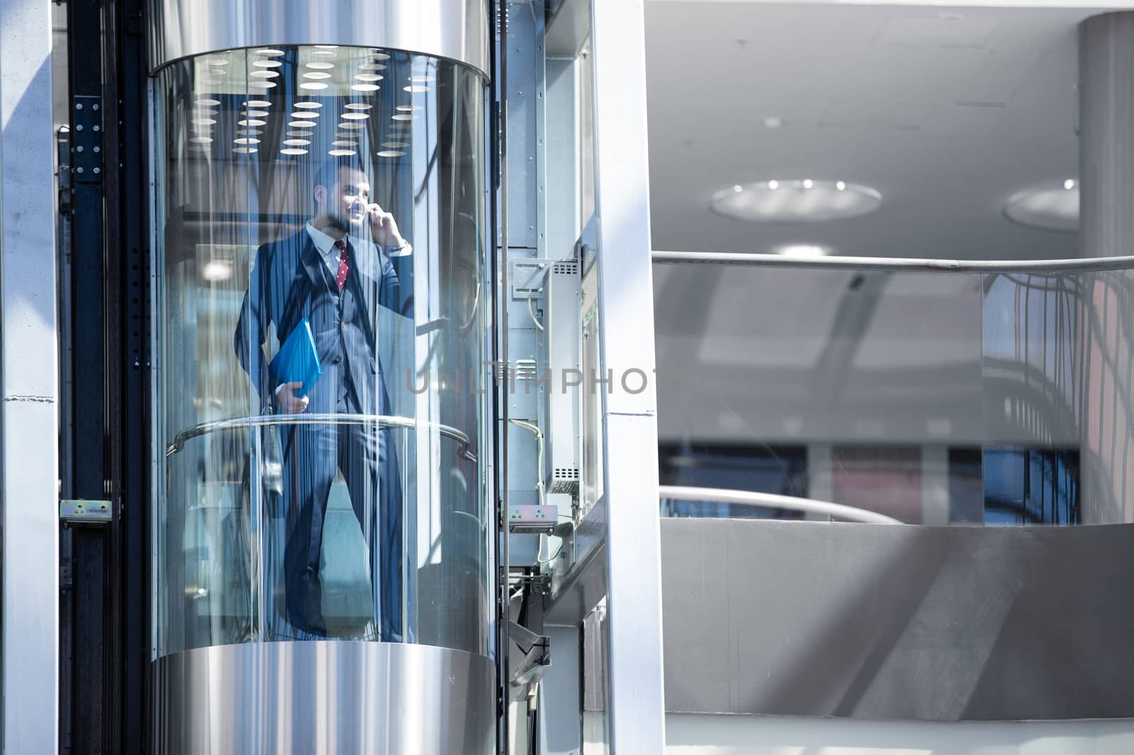 Businessman in modern glass elevator talking by the phone and holding briefcase